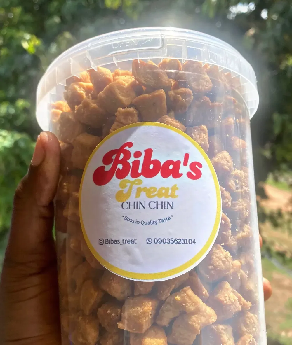 A hand holding up a tub of Biba's Treats chinchin outdoors